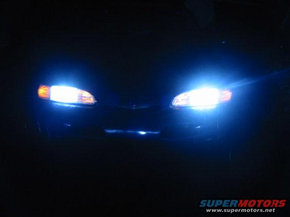 Car headlights on at night. Text at bottom says SUPERMOTORS.NET