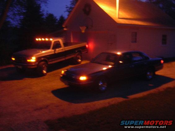 Dark sedan parked in front of a house at night, with a pickup truck behind it