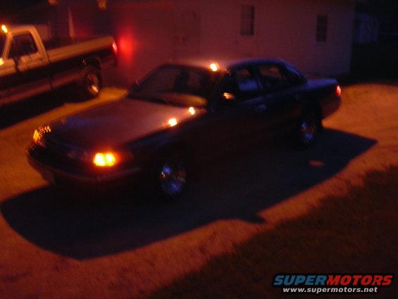 Dark sedan with headlights on, parked next to a pickup truck at night