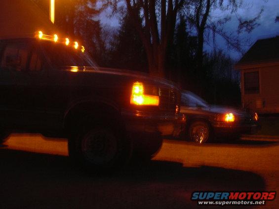 Dark-colored truck with amber cab lights, seen from the front-left at night