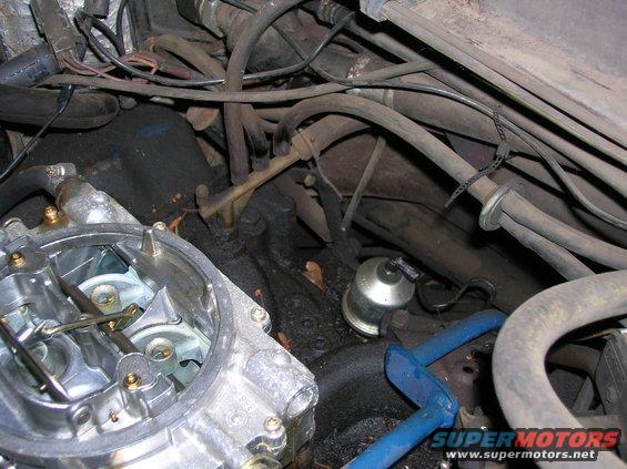 Close-up of a vehicle's engine bay, showing a carburetor and various hoses and wires