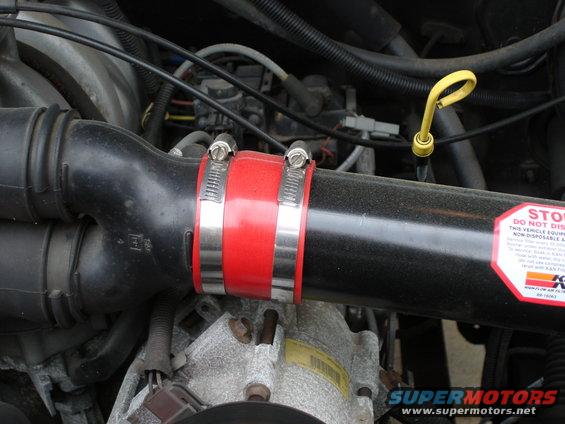 Close-up of a black engine air intake hose with a red silicone coupler and metal clamps. K&N sticker visible