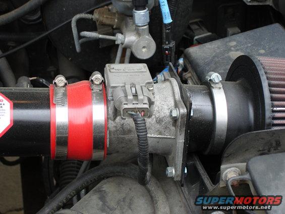 Close-up of a vehicle's engine air intake system with a red hose and a mass airflow sensor