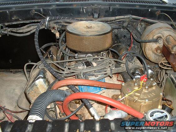 Engine bay with air cleaner, distributor, hoses, and wiring visible. Some text on hoses and distributor cap