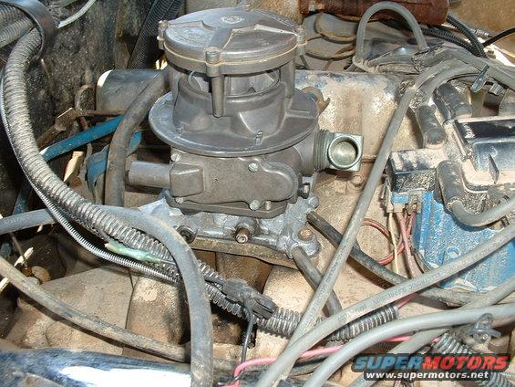 Close-up of a carburetor and engine wiring with various hoses and components