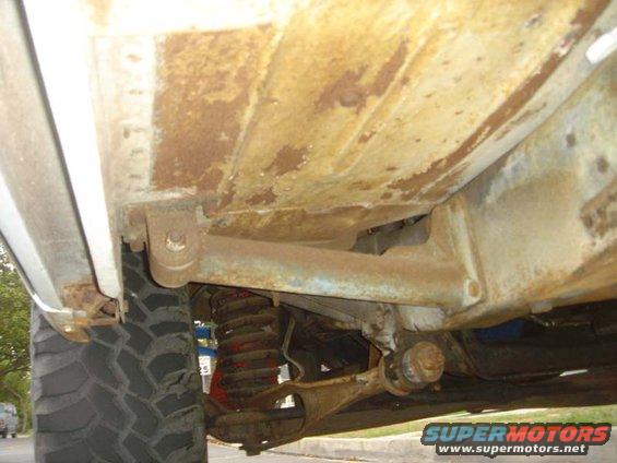 Close-up of rusty undercarriage and suspension components, with a large tire visible