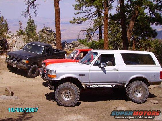 Silver SUV with off-road tires and a two-tone paint job. A black truck and red vehicle are behind it