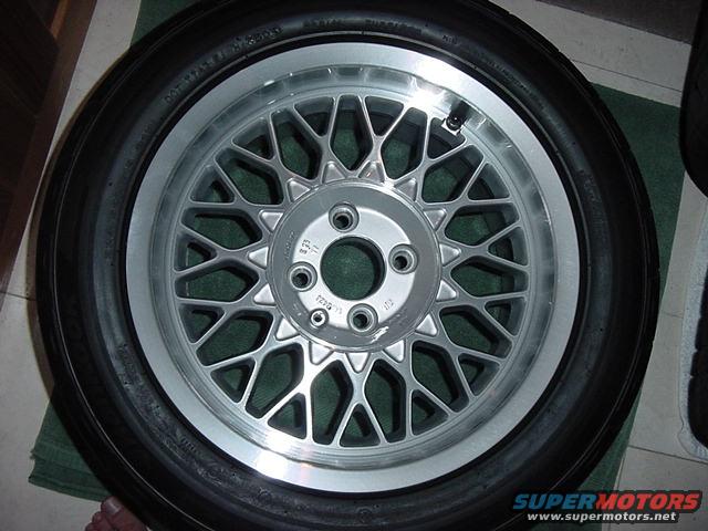 Silver mesh wheel with a black tire, showing a valve stem and lug nut holes