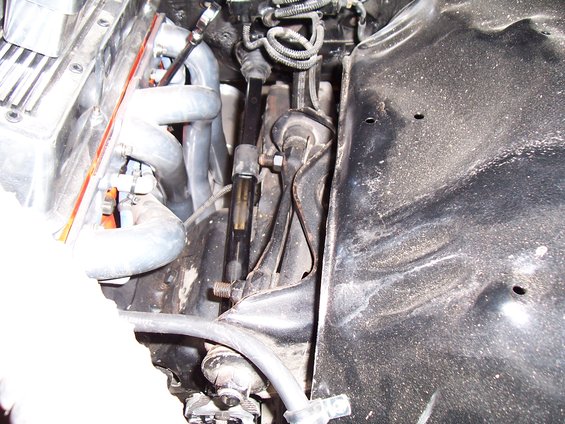 Close-up of engine bay with exhaust manifold, steering linkage, and inner fender well