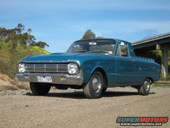 Blue 1964 Ford Falcon Ranchero parked on a dirt road with a bridge in the background
