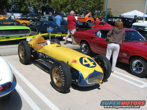 Yellow and blue open-wheel race car with number 4 on the nose, parked next to other cars