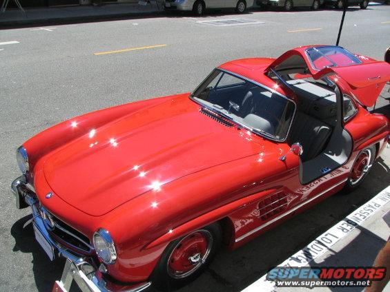 Red gullwing coupe with doors open, parked curbside