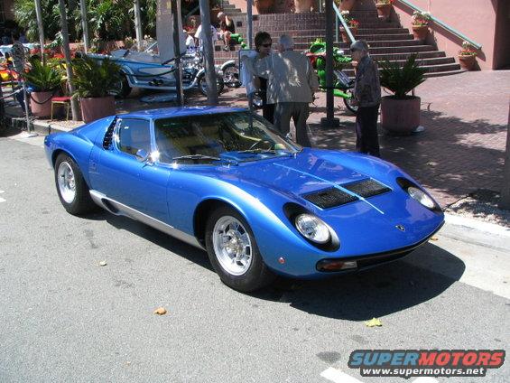 Blue Lamborghini Miura parked on street, people and stairs in background