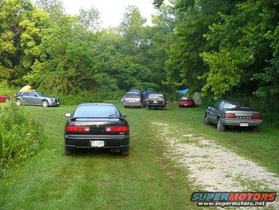 Black coupe with a spoiler parked in a campsite. Other cars and tents are visible in the background