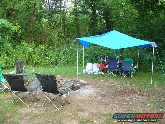Campsite with blue tarp, chairs, and campfire
