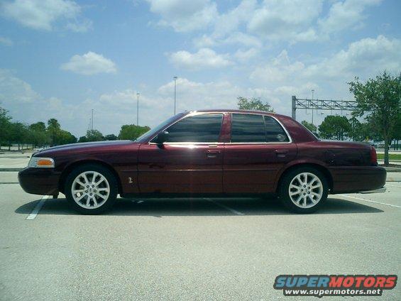Maroon sedan parked on pavement, side view. It looks like a 2004 Ford Crown Victoria