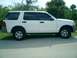 2002 Ford Explorer - Side view of a white 2002 Ford Explorer, parked on a paved surface with grass and trees in the background.