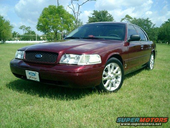 Maroon Ford Crown Victoria parked on grass, front 3/4 view, showing grille and headlights