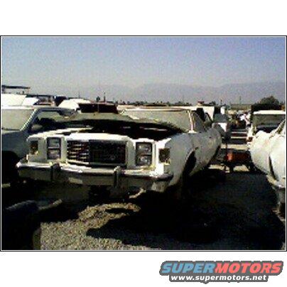 White sedan with hood up in a junkyard, other vehicles visible