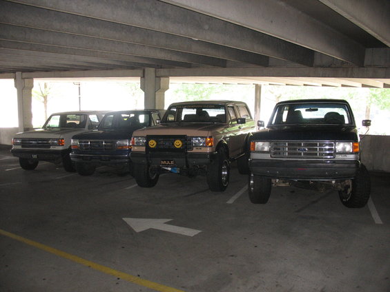 Four Ford trucks parked in a garage, including a 1995 Ford C-350 (Centurion Conversions)