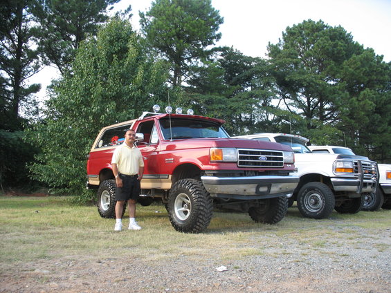 Red Ford Bronco with lifted suspension and off-road tires, parked on grass next to other trucks
