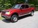 2002 Ford Sport Trac - Red 2002 Ford Sport Trac pickup truck parked on asphalt with trees in background.