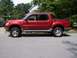 2002 Ford Sport Trac - This red Ford Sport Trac is shown from the side, parked on a paved surface with trees and a house in the background.