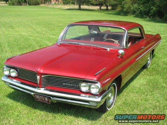 Red vintage coupe with chrome grille and dual headlights parked on a grassy lawn