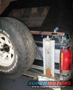 Spare tire mounted on the back of a Ford Bronco, with a Hi-Lift jack attached