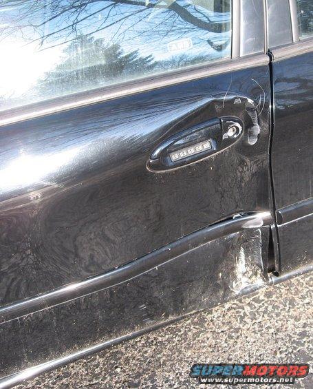 Black car door with dented lower panel and damaged door handle. Keypad entry visible on handle
