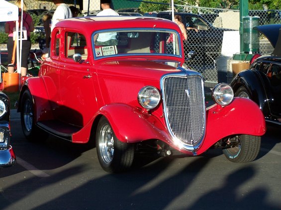 Red coupe hot rod with chrome grille and headlights, parked outdoors