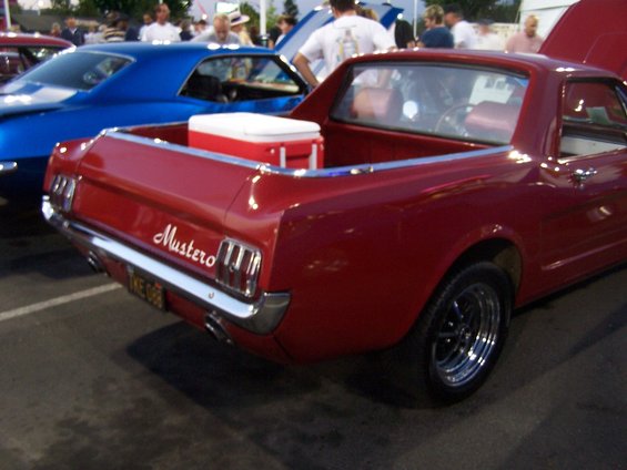 Red coupe utility with 'Mustero' badge, cooler in bed, parked next to blue car