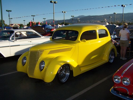 Yellow 1937 Ford hot rod parked next to a white classic car and a red classic car