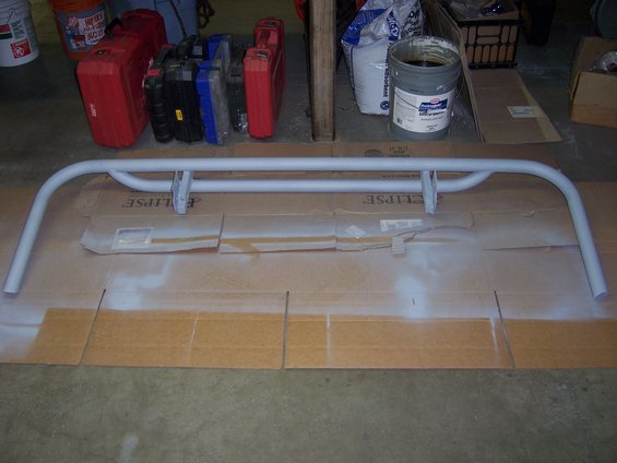 Light gray tubular rear bumper with two mounting brackets, laid on cardboard