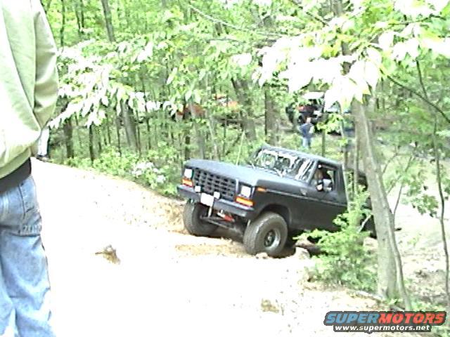 Black 1978 Ford Bronco driving off-road through trees