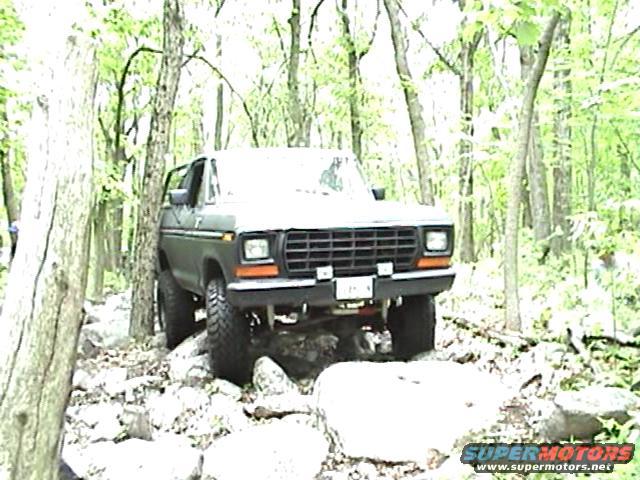 1978 Ford Bronco driving over rocks in a wooded area