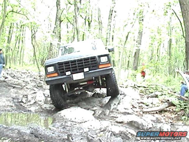 Ford Bronco going over rocks on a trail. It has a black grille and orange turn signals