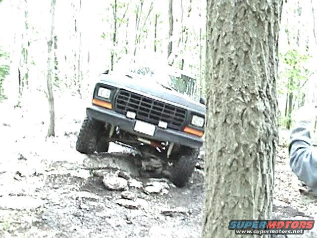 Dark Ford Bronco driving over rocks, front grille and headlights visible