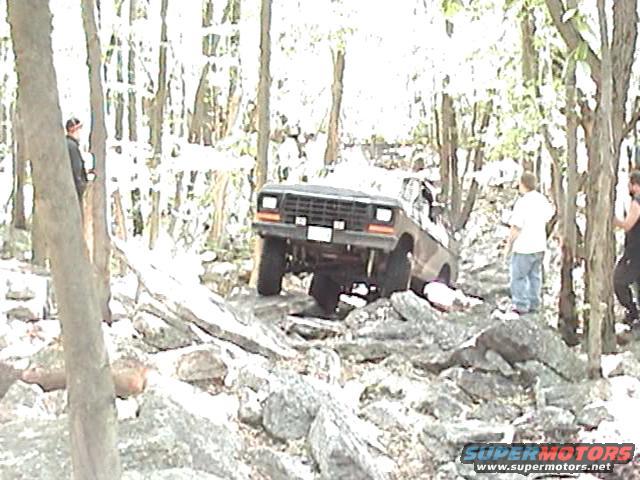 SUV navigating a rocky, wooded trail with people watching