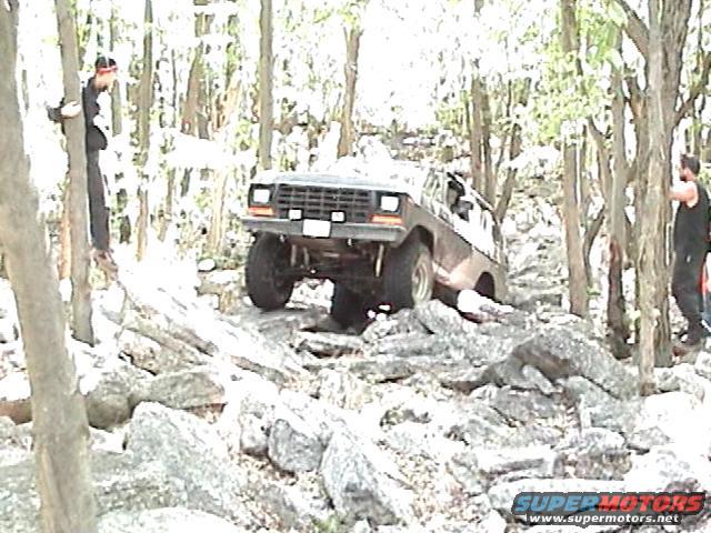 Brown 1978 Ford Bronco navigating a rocky, wooded trail
