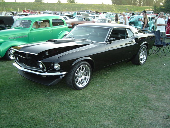 Black 1969 Ford Mustang Mach 1 parked on grass with other cars in background