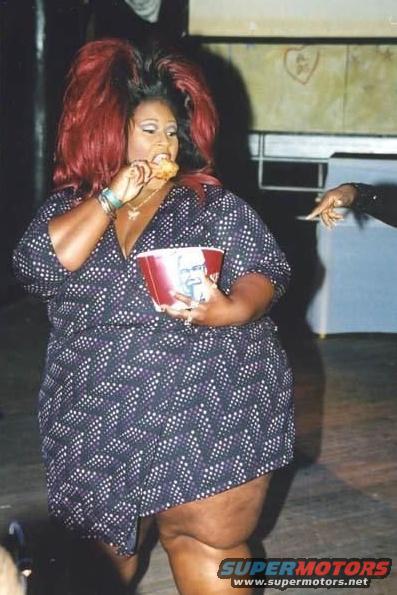 Woman in a patterned dress eating fried chicken from a red bucket
