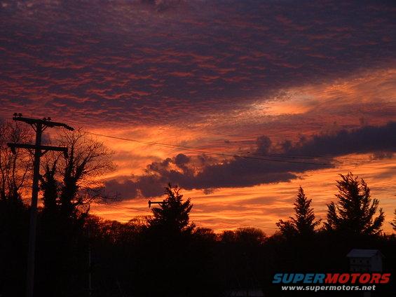 Sunset sky with orange and purple clouds over silhouetted trees and a utility pole