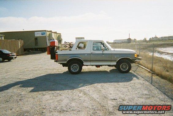 1991 Ford Bronco parked on gravel lot, side view. Spare tire carrier and cooler mounted on rear