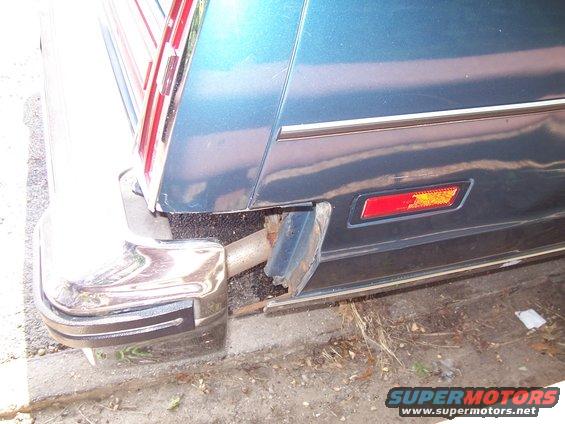 Blue car's chrome bumper and exhaust pipe are visible, with a damaged black plastic trim piece