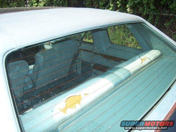 Rear window view of car interior, showing seats and a damaged parcel shelf with a faded graphic