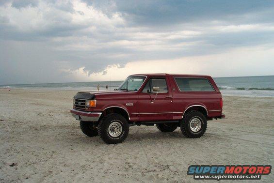 Red 1991 Ford Bronco parked on a beach with the ocean in the background