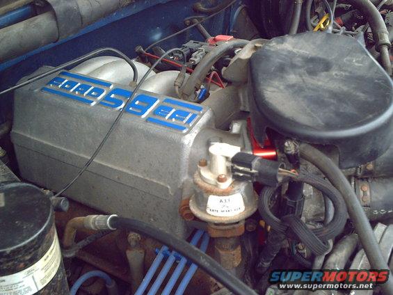 Aluminum intake manifold with blue 'Ford' lettering, engine components, and wiring