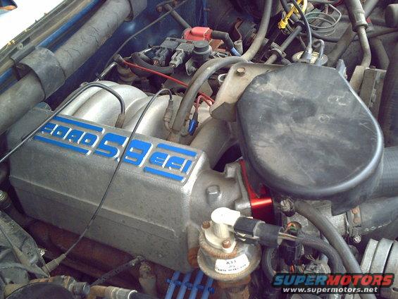 Engine bay with Ford 5.8 EFI intake manifold, blue lettering, and various hoses and wires