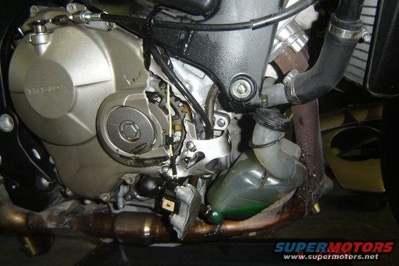Close-up of a damaged motorcycle engine, showing broken casing and exposed wires